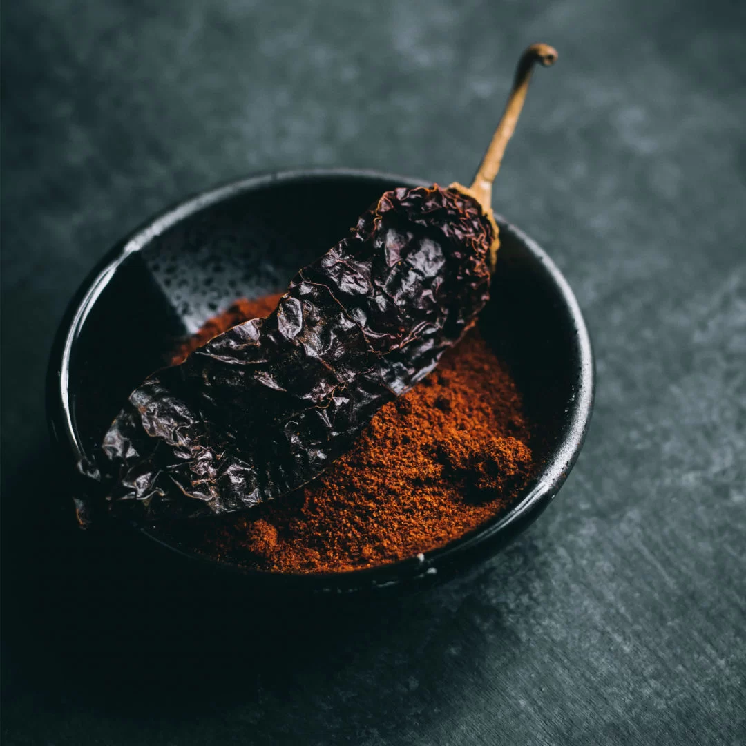 a small bowl of paprika sits with a large dried pepper on top.