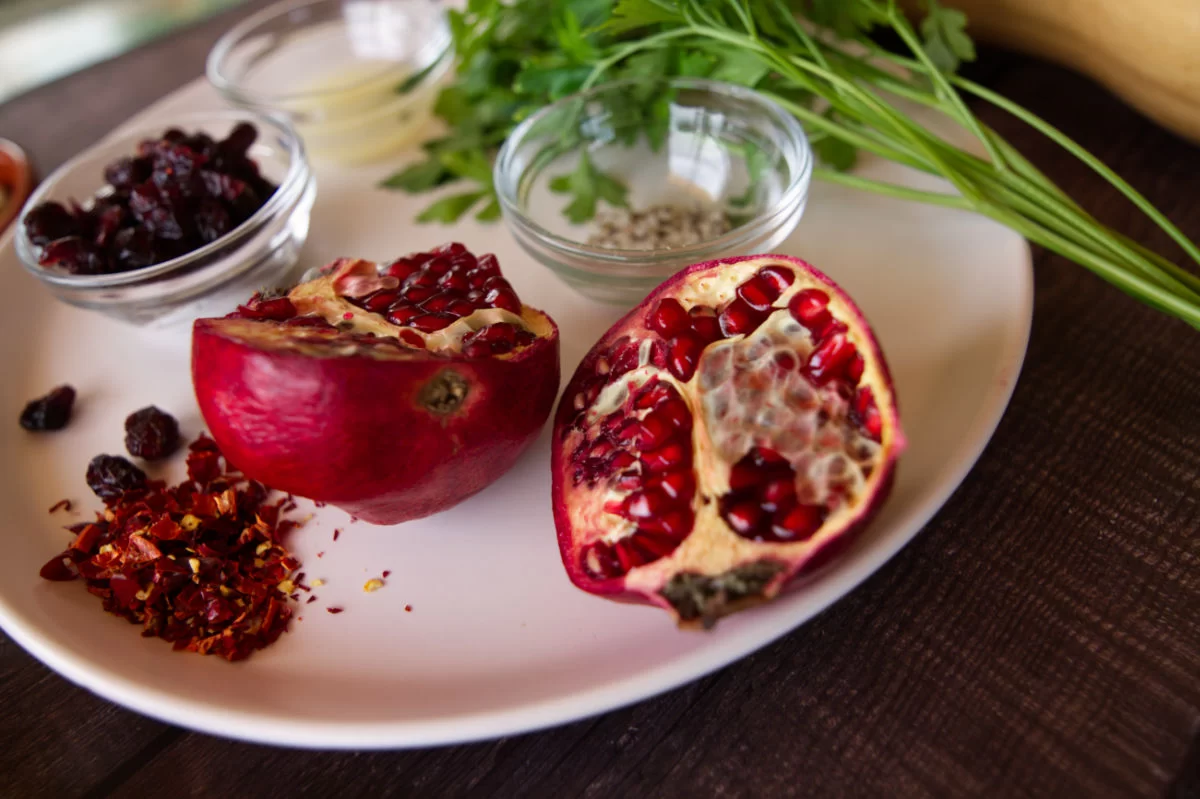 A fresh pomegranate is browkn open on a plate beside some chili flakes salt and fresh parsley
