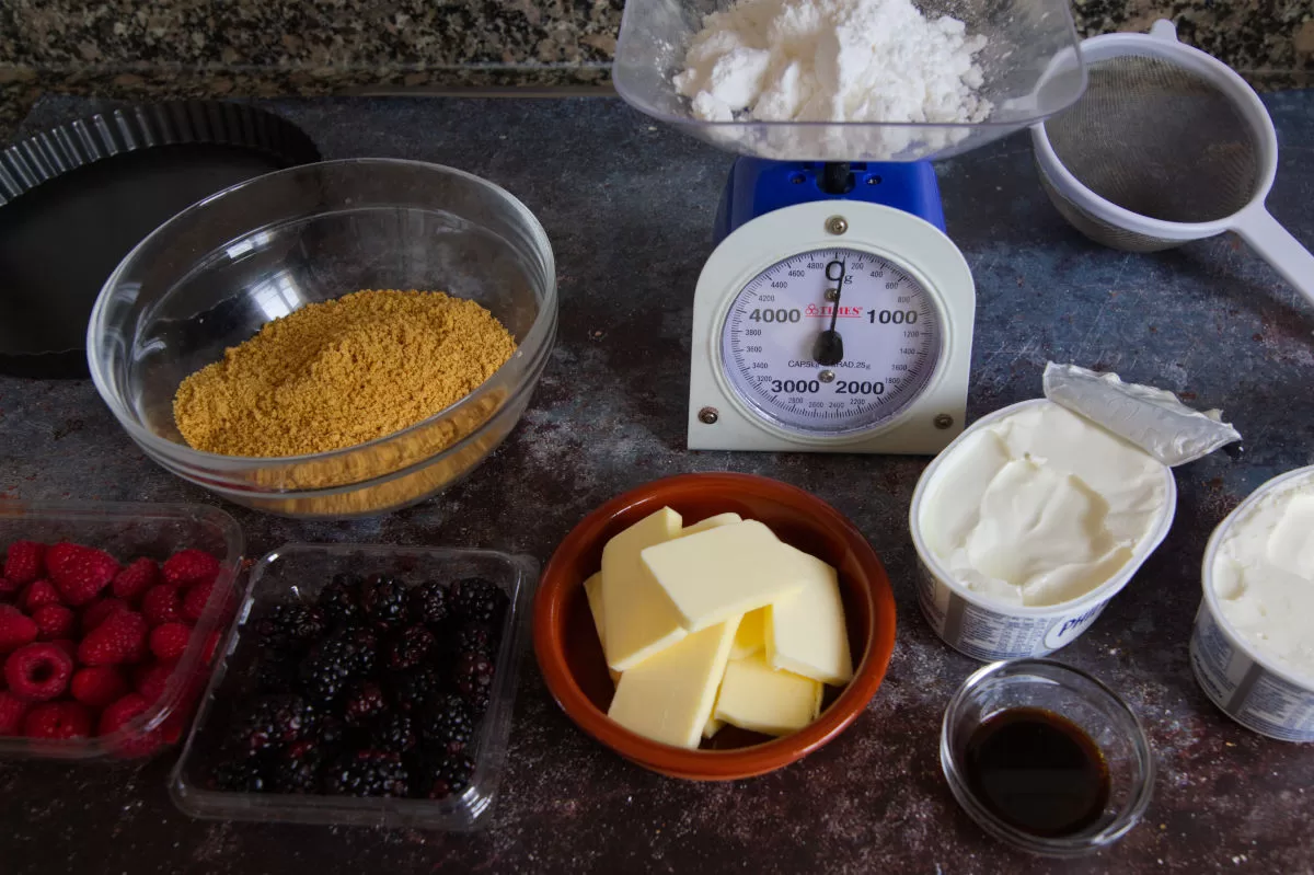 ingredients for making a mixed berry cheesecake are laid out on a kitchen counter