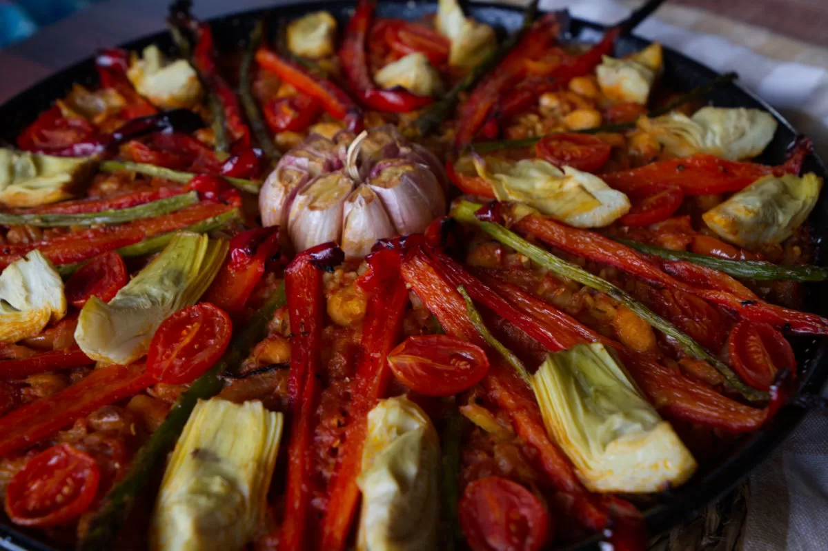 a large pan of vegan arroz al horno is topped with roasted red pepper and a whole head of garlic