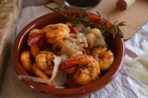 A bowl of Spanish garlic Shrimp sits beside a wedge of Manchego cheese.