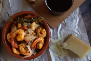 A bowl of Spanish garlic Shrimp sits beside a wedge of Manchego cheese