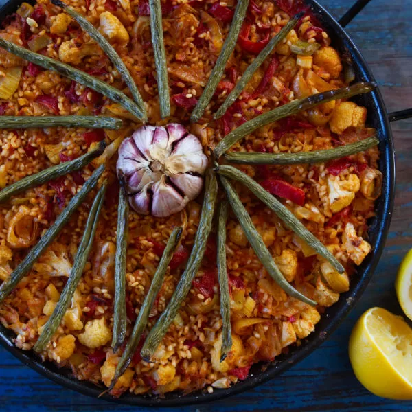 A large pan of Spanish oven-baked rice is decorated with a head of garlic and some roasted green beans