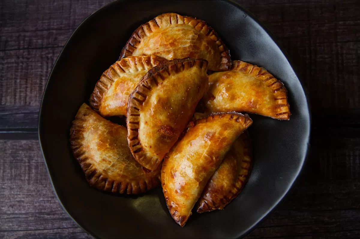 a black bowl is filled with baked empanadas with fish and romesco sauce filling.