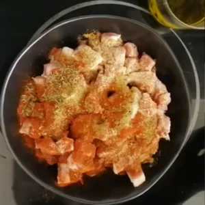 herbs and spices are added to a bowl of diced pork.