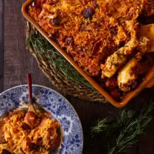 A large dish of spicy chicken, chorizo, and ricce sits beside a small bowl serving