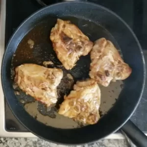 4 browned chicken thighs in a pan.