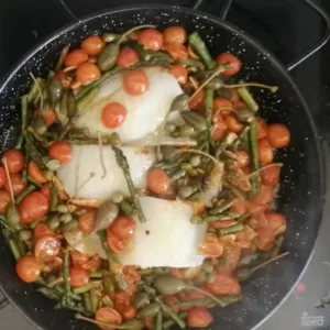 cod fillets are added to a pan of sauteed asparagus and cherry tomatoes