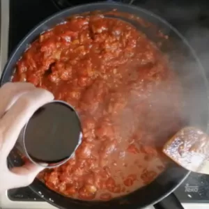 A glass of red wine is added to a rich red sauce
