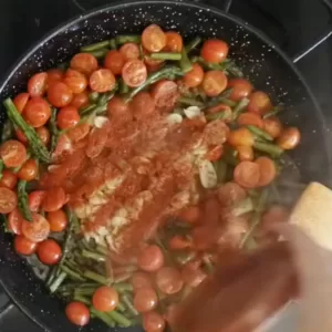 Spices are added to a pan of simmering vegetables.