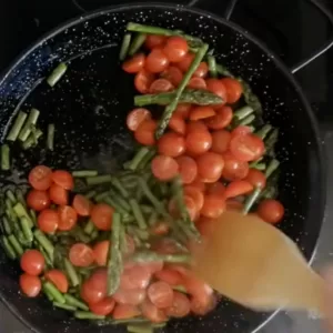 Tomatoes are added to a pan of sauteed asparagus.