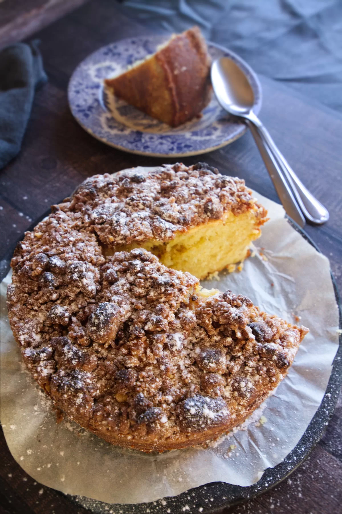 An apple cake is dusted with icing sugar and a slice is served