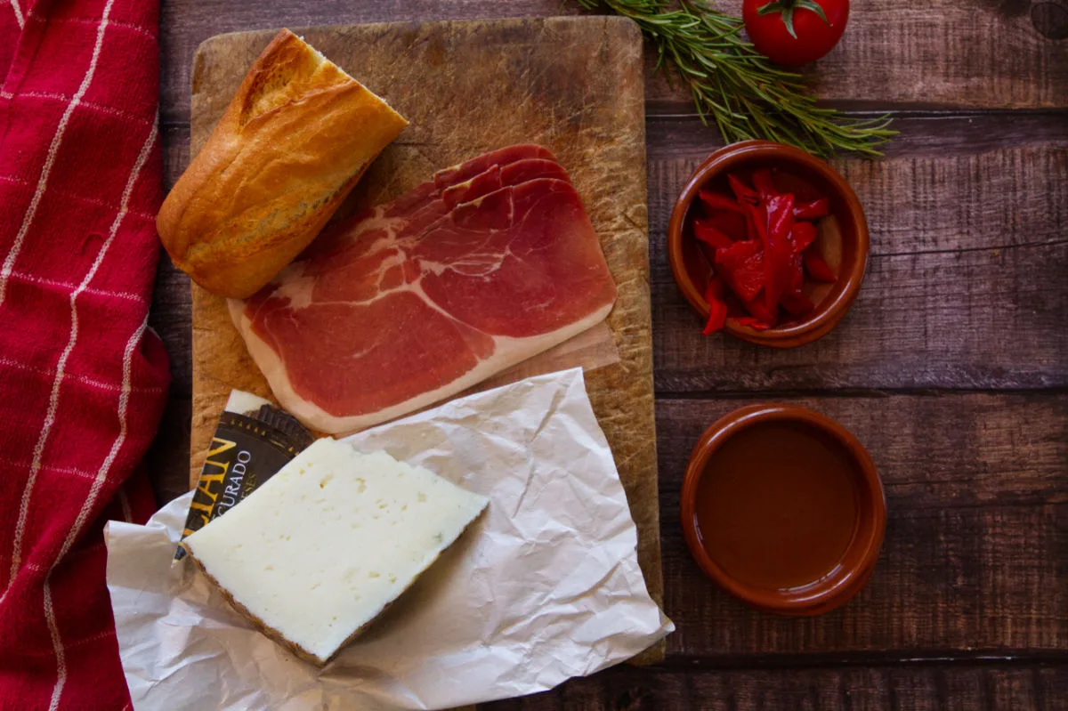 Ingredients for making a ham and mahcego cheese bocadillo are laid out on a kitchen table