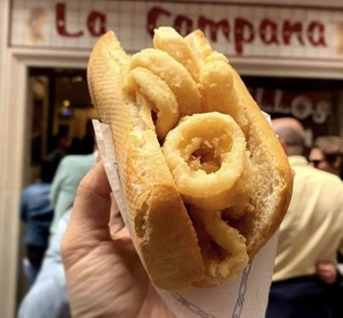 A bocadillo with calamary is help up in front of the famous restaurant La Campana in Madrid