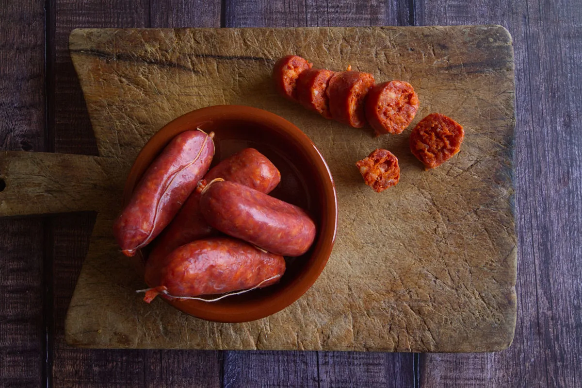 A bowl or red chorizo sausage sits next to some sliced chorizo pieces