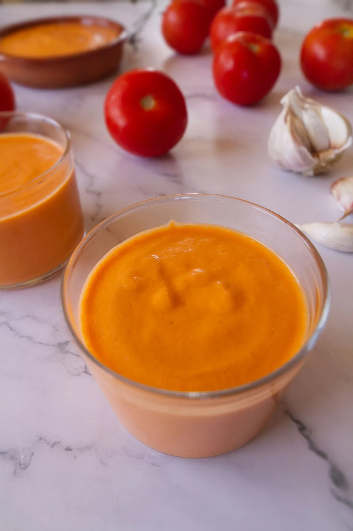 A small glass of vegan salmorejo sits beside some ripe red tomatoes. 