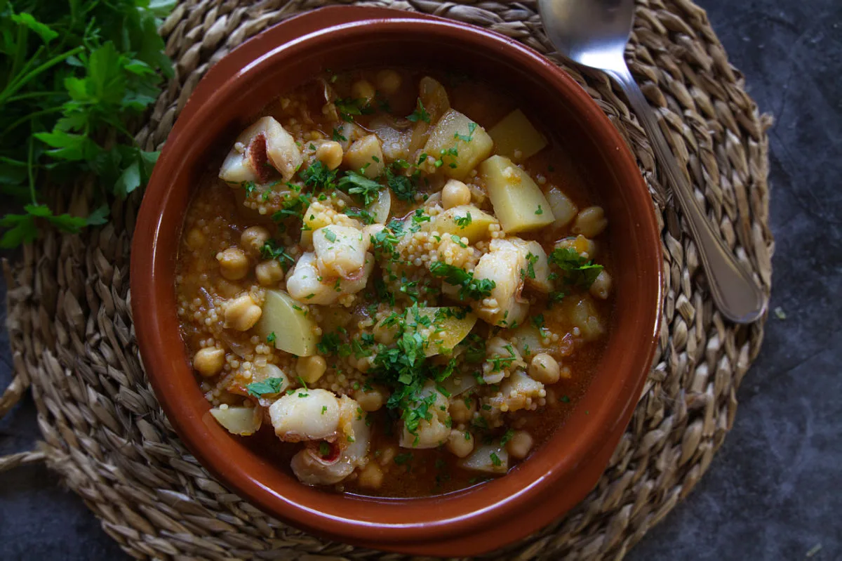 A small cermaic bowl of maravilla fish stew sits beside a bunch of fresh parsley.