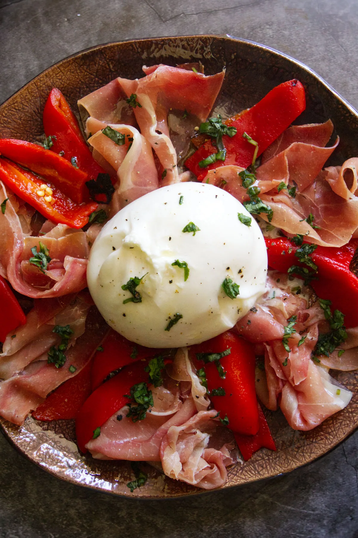 A plate of Burrata with serrano ham and roasted peppers.