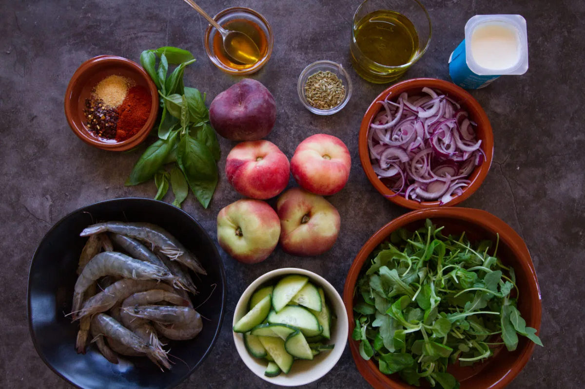 ingredients used to make spicy grilled shrimp with tangy peach salad are laid out on a table.