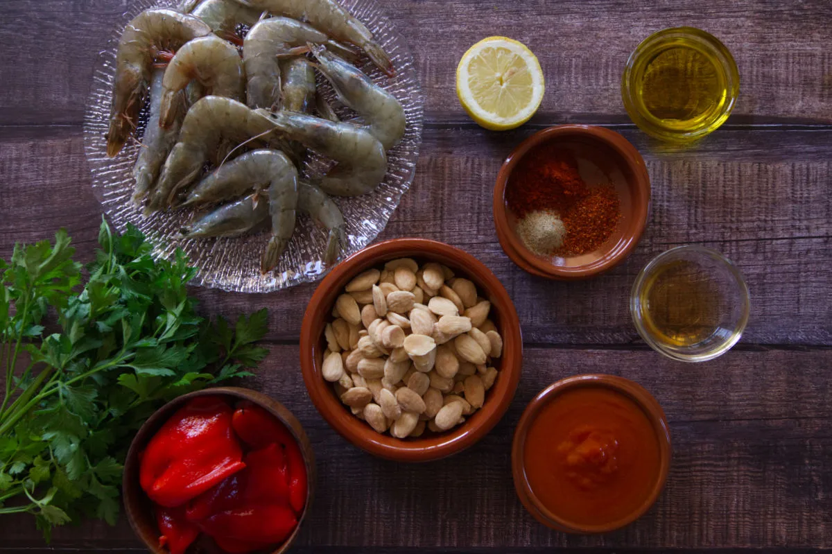 a plate of shrimp sit beside other ingredients and spices used to make pan-fried spicy Shrimp with romesco sauce.