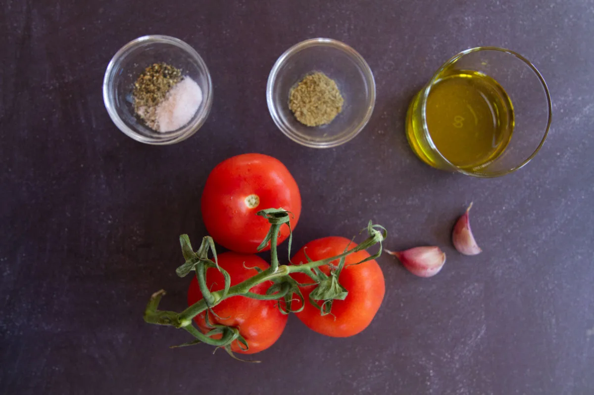 Vinne tomatoes, garlic, olive oil, and salt and pepper sit on a counter top. 