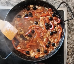 Some black olives and white beans are added to a pan of simmering veggies.