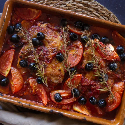 A large casserole dish of Mediterranean boneless chicken thighs with a rich red sofrito sauce.