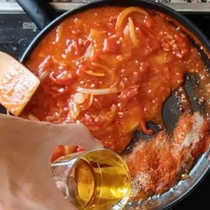 Spices are added to a pan of simmered onions, garlic, and tomatoes.