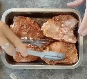 Chicken thighs are turned in a baking tray with some marinade.