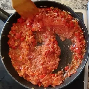 A pan of sofrito sauce simmers on a stovetop.