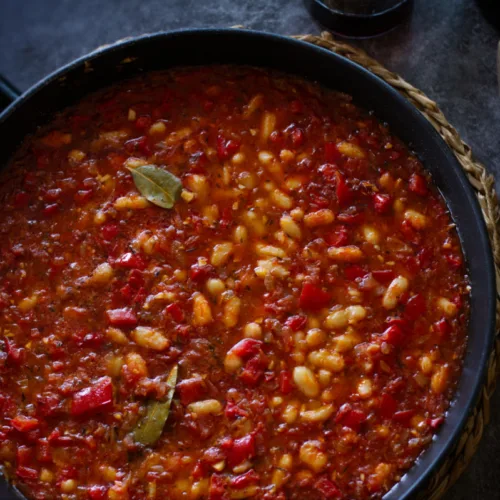 a large pan of white bean stew sits with a few bay leaves on top.