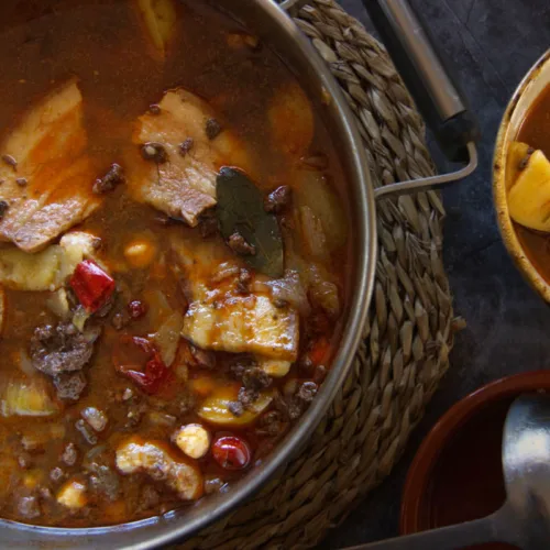 A large pot of spicy Spanish-style pork stew is served to a small bowl.