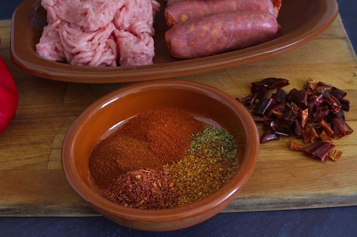 Some ground chicken mince sits beside some chorizo sausage, spices,and dried chili.