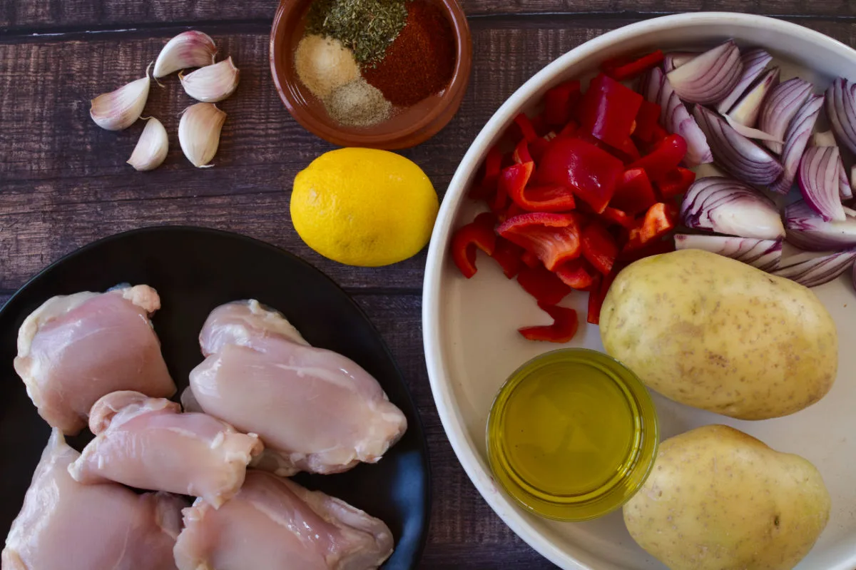 Chicken thighs sit beside some potatoes, red pepper, and spices. 