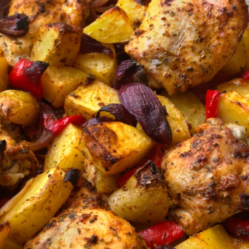 A large dish of cooked chicken thighs and roasted potatoes.