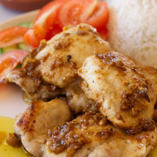 garlic-infused chicken thighs sit on a plate beside some steamed rice and salad.