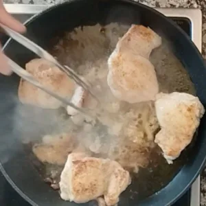 Chicken thighs simmer in a pan with some garlic, sherry, and water.