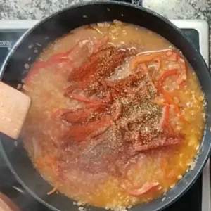 Spices are added to a pan of sauteed onion and red bell pepper.