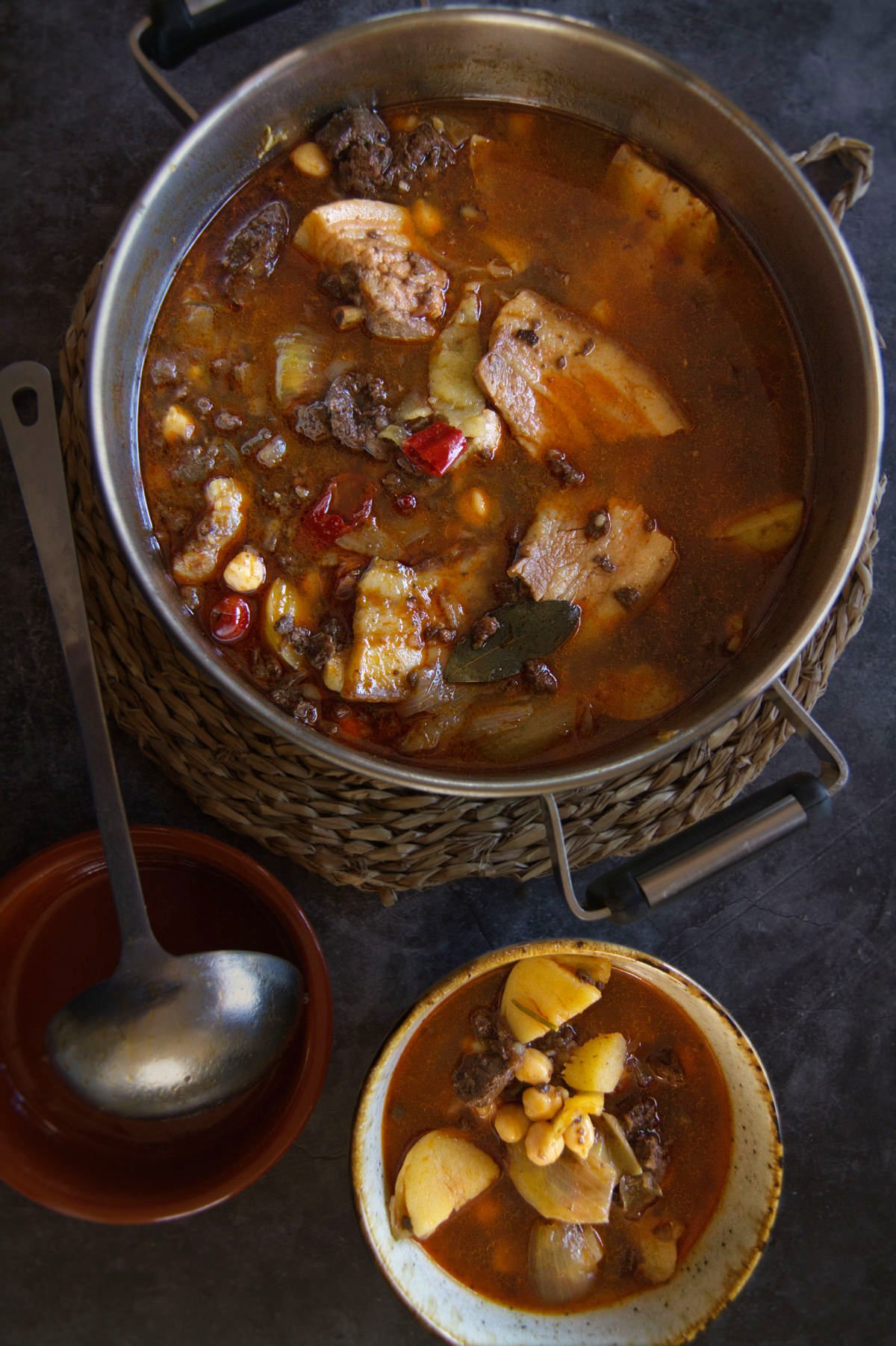 A large pot of spicy Spanish-style pork stew is served to a small bowl.