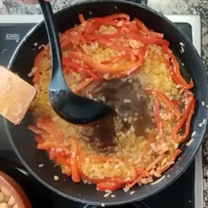 chicken stock is added to a pan with sauteed onion and red bell pepper.