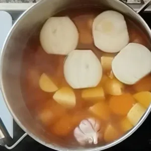 potatoes, onions, and garlic are added to a large pot with some stock.