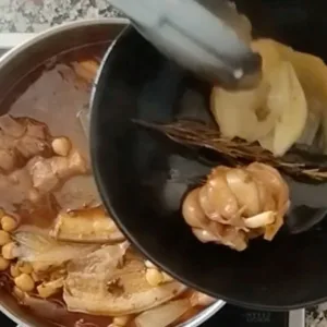 A head of garlic and simmered onion are removed from the stew.