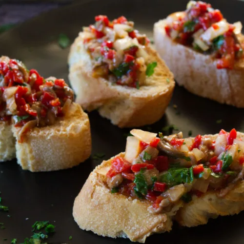 A plate of anchovy and pepper spread on some slices of toasted bread.