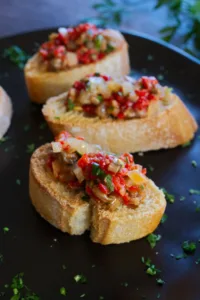 A plate of anchovy and pepper spread on some slices of toasted bread.