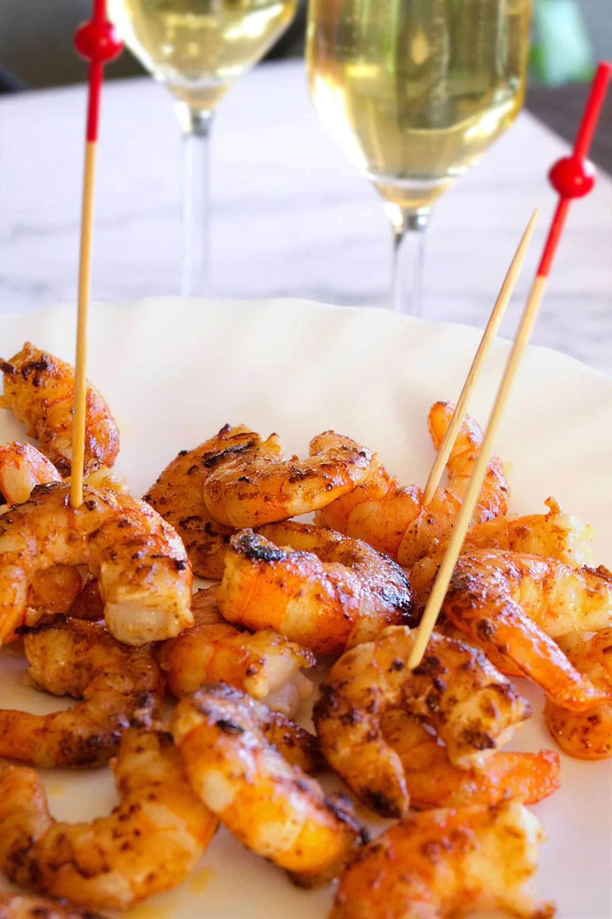 Some cooked shrimp on skewers sit beside two glasses of Cava.