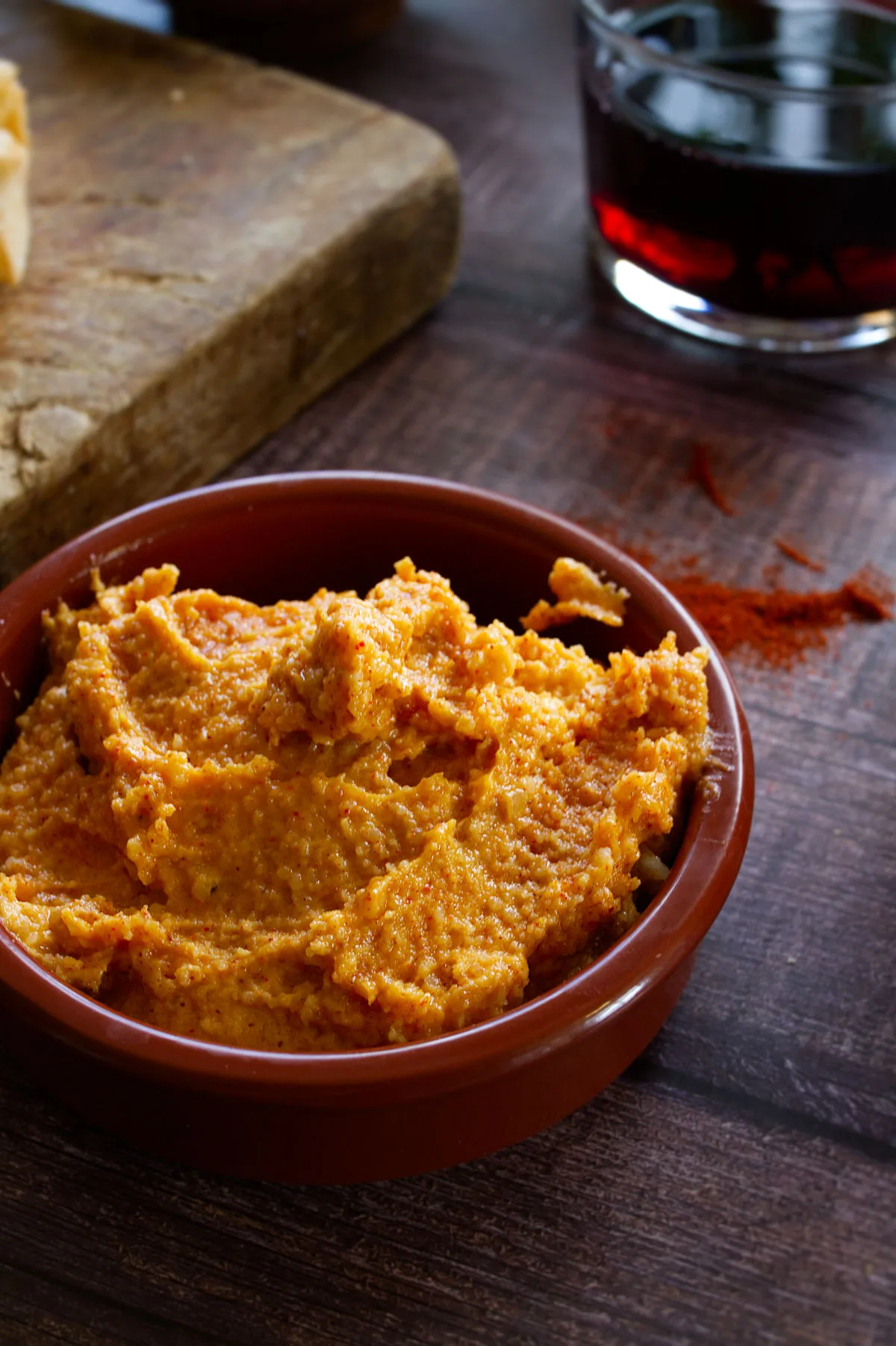 A bowl of Almogrote spiced cheese dip sits beside some slices of bread and some red wine.