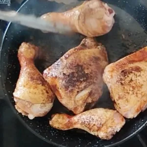 Chicken pieces cook in a pan.