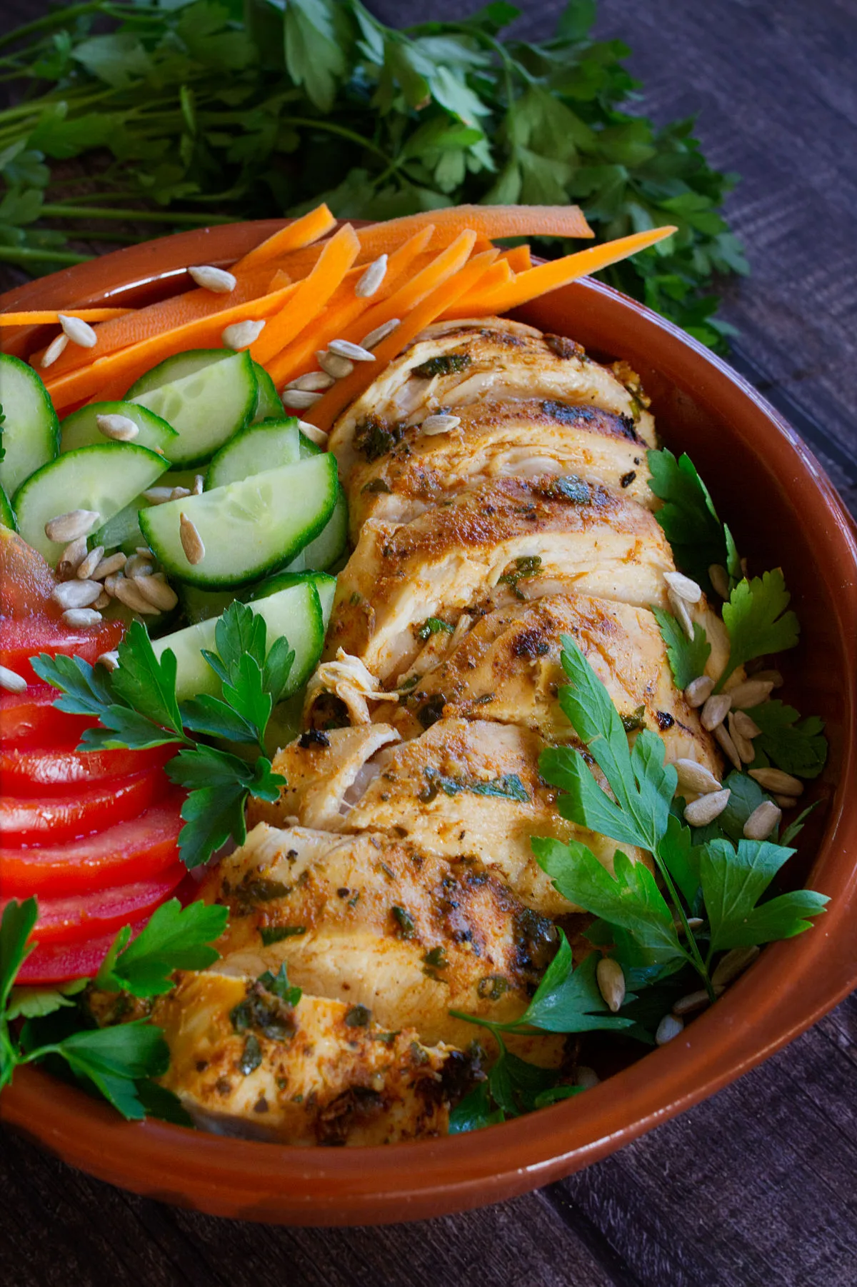 Slices of grilled Mediterranean chicken breast sit in a bowl with some salad.