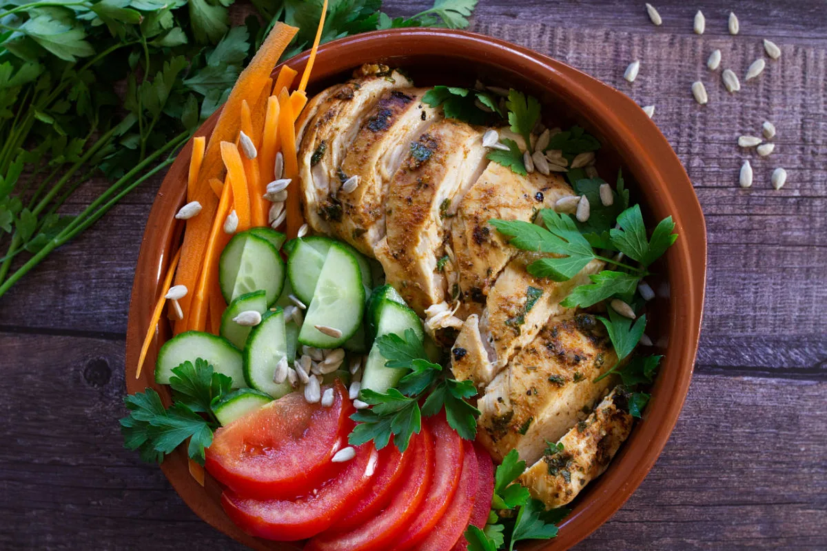 Slices of grilled Mediterranean chicken breast sit in a bowl with some salad.