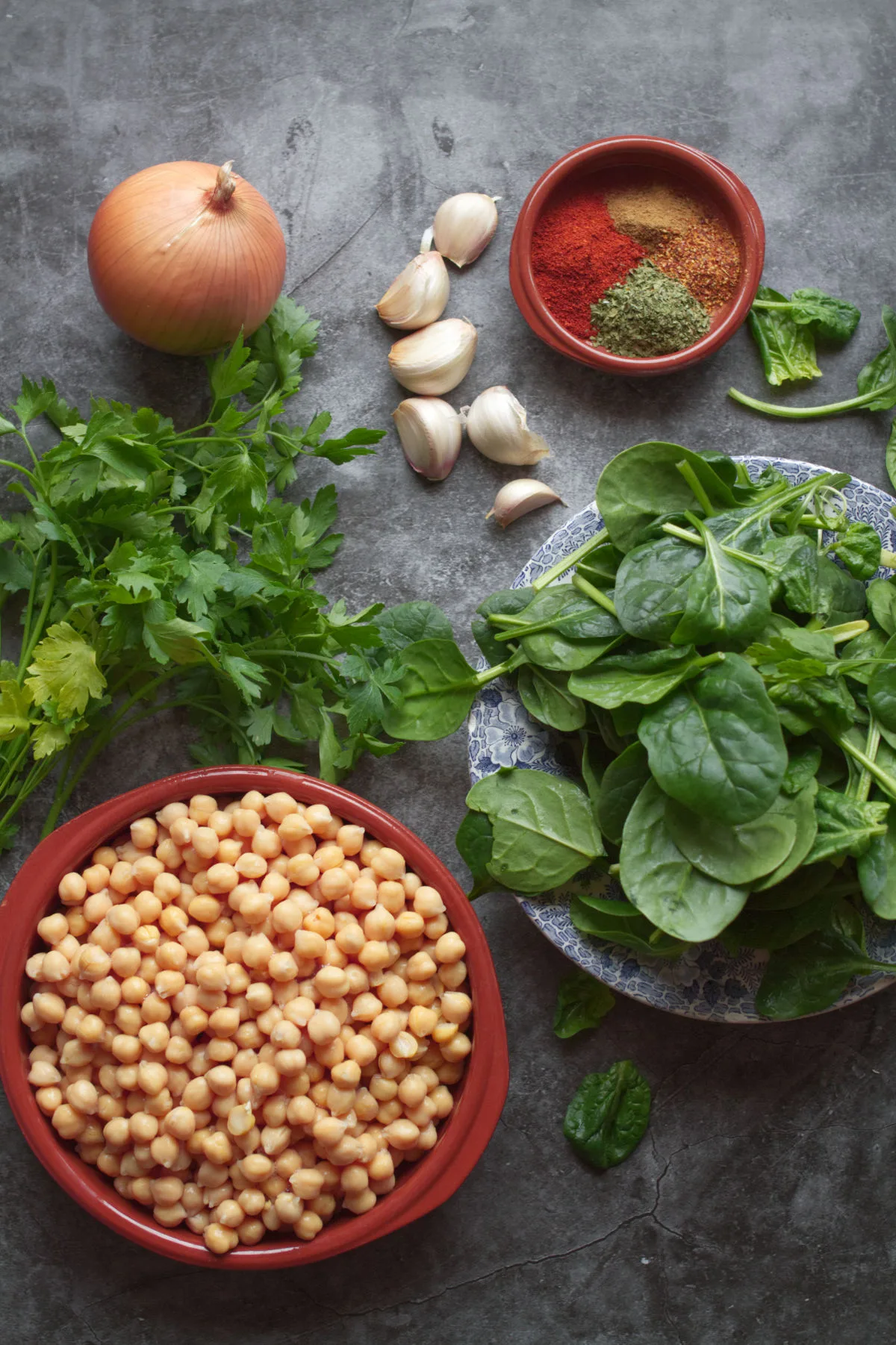 A alrge bowl of chickpeas sists beside a bowl of spinach, onion, garlic, and some herbs and spices.